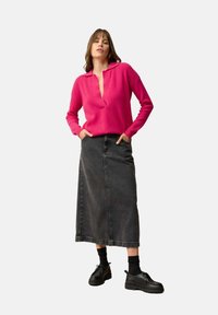 Fuchsia gestrickter Pullover mit Kragen, kombiniert mit einem schwarzen Denim-Maxikleid und schwarzen Schnürschuhen. Strukturiert und lässiger Stil.