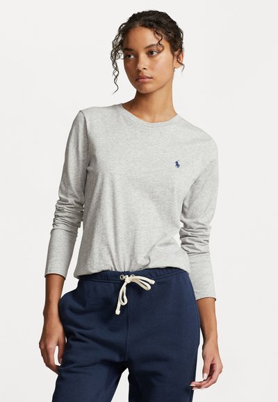 T-shirt gris à manches longues en tissu doux, avec un col rond et un petit logo bleu marine. Associé à un pantalon de jogging bleu marine à cordon de serrage.