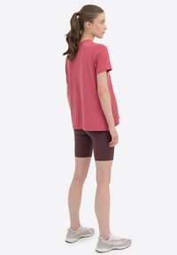 Maglietta rosa a maniche corte e dal taglio morbido abbinata a pantaloni corti bordeaux. La maglietta ha una texture liscia, mentre i pantaloni sono aderenti.