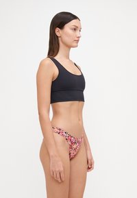 Črn skrajšan top s širokimi ramnicami, v kombinaciji z rožnatimi cvetličnimi bikini hlačkami, ki imajo nizek pas in gladko teksturo. Enostavni in živahni vzorci.