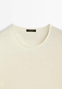 Pull tricoté de couleur crème avec un col rond et une étiquette noire à l'intérieur du col portant la mention "Massimo Dutti Made in China."