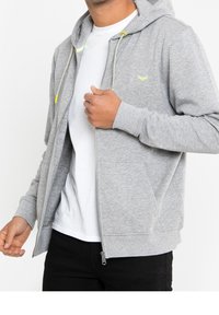 Gray zip-up hoodie with a drawstring hood, contrasting yellow accents, and front pockets, worn over a white T-shirt. Soft texture.