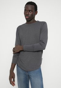 Grijze longsleeve t-shirt met een ronde halslijn en een licht gebogen onderkant, gemaakt van een zachte, rekbare stof. Voorzien van aansluitende mouwen.