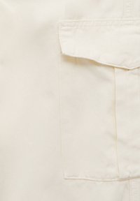 Tissu crème à la texture lisse et à la trame diagonale, présentant une poche à rabat et des coutures soignées le long des bords.