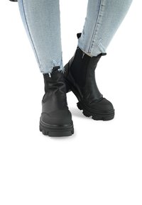 Schwarze Leder-Stiefeletten mit strukturierter Oberfläche, elastischen Seitenpanelen und robusten Gummisohlen, getragen mit verwaschenen hellblauen Jeans.