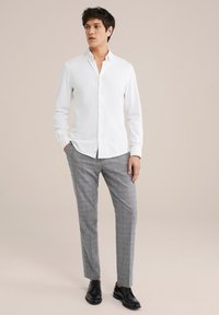 Witte overhemd met lange mouwen, gecombineerd met grijs geruite broek. Zwarte veterschoenen maken de look compleet.