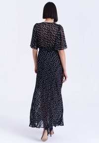 Czarna maxi sukienka w białe kropki z krótkimi falbaniastymi rękawami, elastycznym pasem, lejącym się materiałem i lekko przezroczystą fakturą.