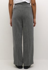 Grijze wijde broek met textuur, voorzien van een hoge taille, subtiele streepjes en twee achterzakken. Zwarte schoenen zichtbaar aan de onderkant.