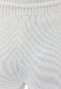 Witte ribgebreide stof met een rekbare tailleband. De textuur is glad met fijne verticale lijnen en subtiele stikdetails.