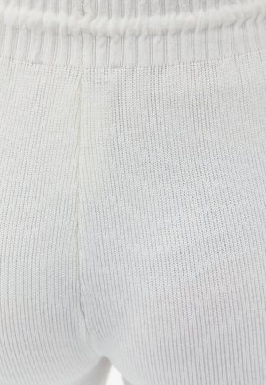 Tessuto a maglia bianco a coste con una cintura elastica. La texture è liscia con sottili righe verticali e dettagli di cucitura discreti.
