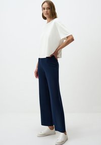 Witte top met korte mouwen, gecombineerd met marineblauwe wijde broek en witte sneakers. Gladde stof met een ontspannen pasvorm en minimalistisch ontwerp.