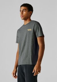 Tmavomodré tričko s krátkym rukávom a zaobleným výstrihom, na ľavej prednej strane zlatým textom "RED BULL RACING". Jednoduchý dizajn a jemná textúra.