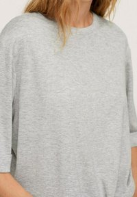 Femme portant un pull léger gris clair uni à manches courtes, col rond et coupe ample.