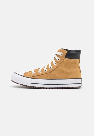 Baskets montantes en daim beige avec lacets blancs, col matelassé noir et semelle en caoutchouc blanche avec bande noire, vues de côté.