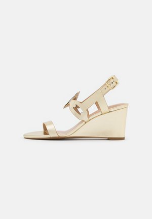 Goldene Wedge-Sandaletten mit Slingback-Design, glattem metallic Material, offener Zehenpartie und Ausschnitten am oberen Riemen.