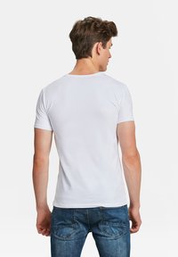 Witte katoenen t-shirt met korte mouwen, met een ronde hals. De achterkant toont een slim fit ontwerp en een gladde textuur. Draagt met een blauwe spijkerbroek.