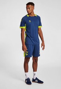 Marineblaue Sporttrikot und Shorts mit leuchtend grünen Akzenten, aus leichtem Material gefertigt. Mit einem Logo und Chevron-Mustern auf den Shorts.