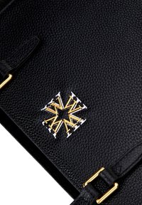 Bolso de cuero negro texturizado con herrajes dorados y plateados. Diseño de emblema notable con elementos geométricos en el centro.