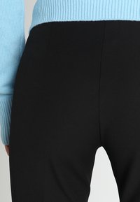 Zwarte high-waisted leggings worden gecombineerd met een lichtblauwe geribbelde trui. De texturen zijn glad met een aansluitend ontwerp.