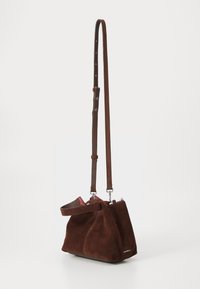 Geantă din suede maro, cu o textură moale, dotată cu o curea detașabilă și accente din metal argintiu, având o formă ușor rotunjită.