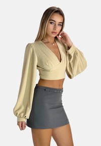 Beige kort topp med djup V-ringning och plisserade detaljer, i kombination med en grå minikjol med bälte och slät yta.