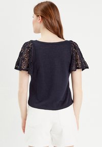 Navy blauwe t-shirt met een ronde halslijn en korte mouwen met kantafwerking; gemaakt van zacht, lichtgewicht materiaal.