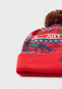 Κόκκινο πλεκτό σκουφάκι με πράσινο πομ πομ, με σχέδιο σε ταινία μπλε, λευκή και πράσινη με τάρανδους και το κείμενο "JUST.".
