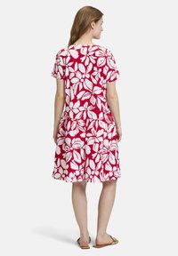 Rotes Blumendruckkleid mit kurzen Ärmeln, gestuften Bund und weichem Stoff. Weiße, übergroße Blumenmuster bedecken das Design. Rückansicht dargestellt.