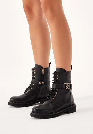 Black leather ankle boots with lace-up front, side zipper, buckle accent, and textured sole. Features gold-tone hardware details.