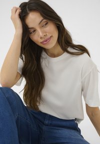 Cremefarvet, kortærmet t-shirt lavet af glat stof, parret med højtaljede blå denimbukser. Simpelt, afslappet fit design.