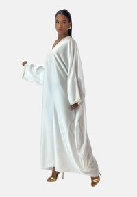 Lang hvid satin kaftan kjole med V-hals og guldkante. Har løse ærmer, flydende silhuet og glat tekstur.
