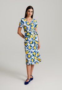 Blumenkleid mit weißem Grund, gelben Zitronen und blauen Blattmustern. V-Ausschnitt, kurze Ärmel und eine Taillenschnürung.