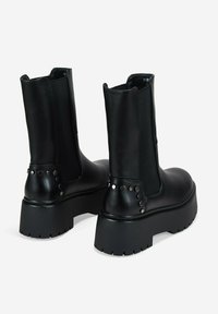 Black leather ankle boots with a chunky platform sole, featuring elastic side panels and metallic stud accents on the heel.