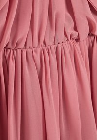 Tissu en chiffon rose avec des plis froncés créant une texture fluide. Le design présente une taille décontractée. Aspect doux et léger.