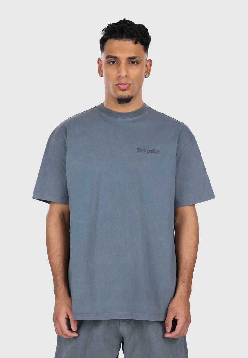 Grå bomulds t-shirt med korte ærmer, rund halsudskæring og et diskret broderet logo på brystet. Glat tekstur, afslappet pasform.