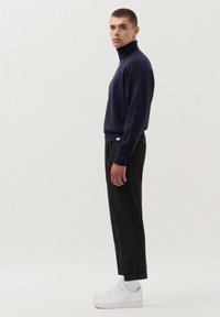 Granatowy sweter z golfem o luźnym kroju, zestawiony z czarnymi spodniami i białymi trampkami, ukazujący proste linie i minimalistyczny design.