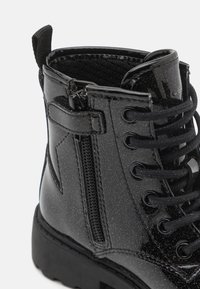 Bottines noires en cuir verni avec une surface texturée, fermeture éclair décorative, lacets ronds et semelle en caoutchouc robuste.