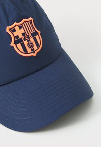 Marineblauw honkbalpet met een geborduurd oranje FC Barcelona-embleem. Het ontwerp heeft een gebogen klep en textiel met textuur.