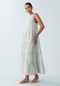 Gelaagde maxi-jurk van lichte stof met verticale strepen, voorzien van een mouwloos ontwerp. Lichtgrijze en witte kleuren met subtiele blauwe accenten.