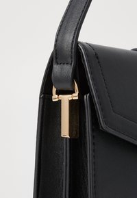 Bolso de mano de piel negra con un diseño estructurado, que presenta un cierre de metal dorado y una correa texturizada. Realzado con detalles de costura limpios.
