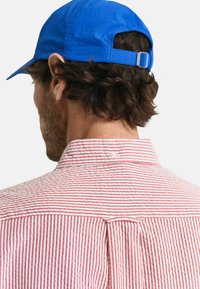 Rood-wit gestreept shirt met een knoopsluiting en een rugplooidetail, gecombineerd met een blauwe pet met een gebogen klep.