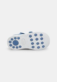 Bērnu apavu zole ar baltu gumiju, ziliem apaļiem satveršanas elementiem, teksturētu dizainu un izcilnēm. Velcro siksna drošai pieguļšanai.