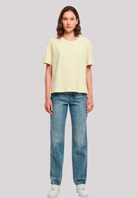 Light yellow cotton t-shirt with short sleeves, relaxed fit, paired with high-waisted light blue denim jeans and white sneakers.