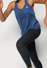 Niebieski sportowy top na ramiączkach z okrągłym dekoltem i logo, w połączeniu z czarnymi legginsami o gładkiej fakturze i dopasowanym kroju.