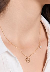 Złoty naszyjnik z wisiorkiem w kształcie serca z napisem "Mummy" oraz małą perłą jako akcentem. Łańcuszek jest delikatny o skręconym wzorze.