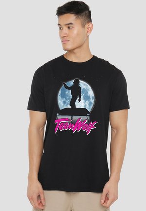 Schwarzes T-Shirt aus Baumwolle mit einem grafischen Design einer Silhouette vor einem Vollmond, mit "Teen Wolf" in fettem pinken Text.