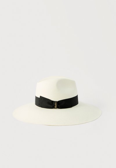 Λευκό καπέλο fedora με φαρδύ γείσο, μαύρη κορδέλα και μικρή χρυσή λεπτομέρεια λογότυπου σε απλό φωτεινό φόντο.