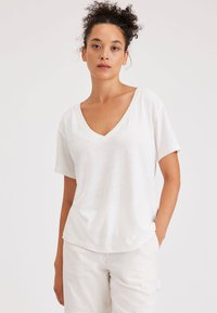 T-shirt bianco in cotone con scollatura a V, maniche corte e vestibilità rilassata. Tessuto testurizzato con un delicato motivo melangiato.