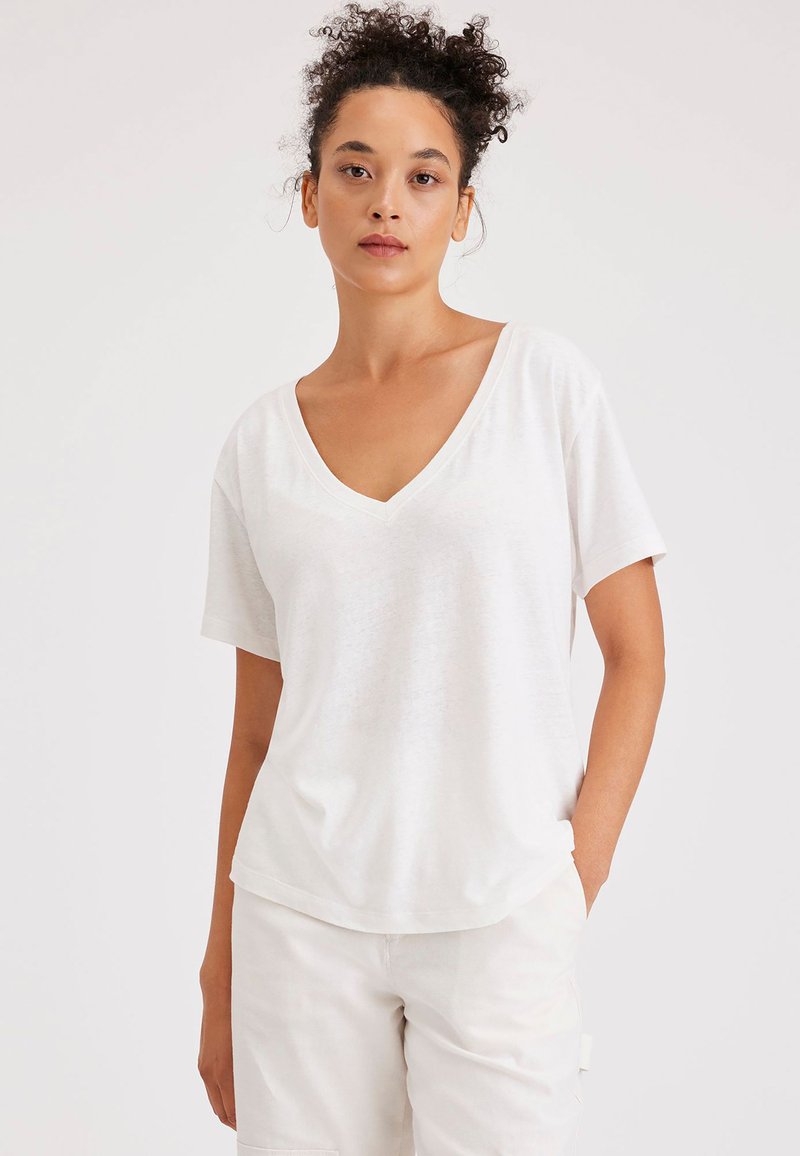 T-shirt bianco in cotone con scollatura a V, maniche corte e vestibilità rilassata. Tessuto testurizzato con un delicato motivo melangiato.