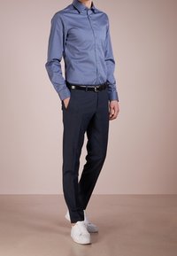 Lichtblauw overhemd met knopen, gecombineerd met donkere, op maat gemaakte broek en witte sneakers. Het overhemd heeft een klassieke kraag en een gladde textuur.